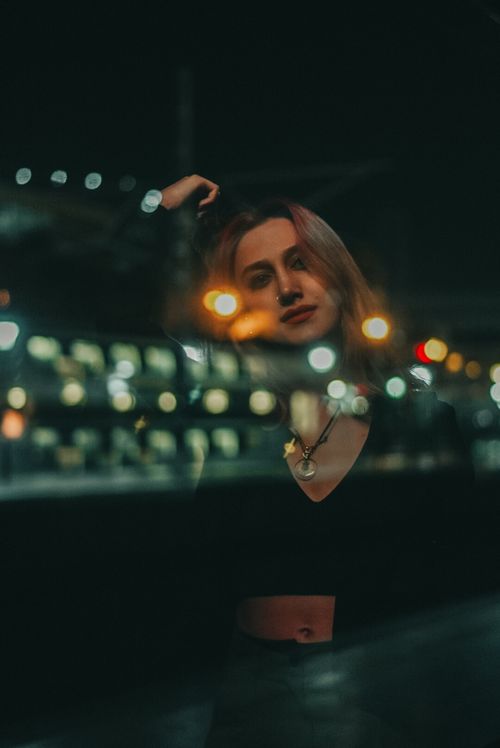Free Artistic portrait of a young woman with urban lights at night, emphasizing a modern dark mood. Stock Photo