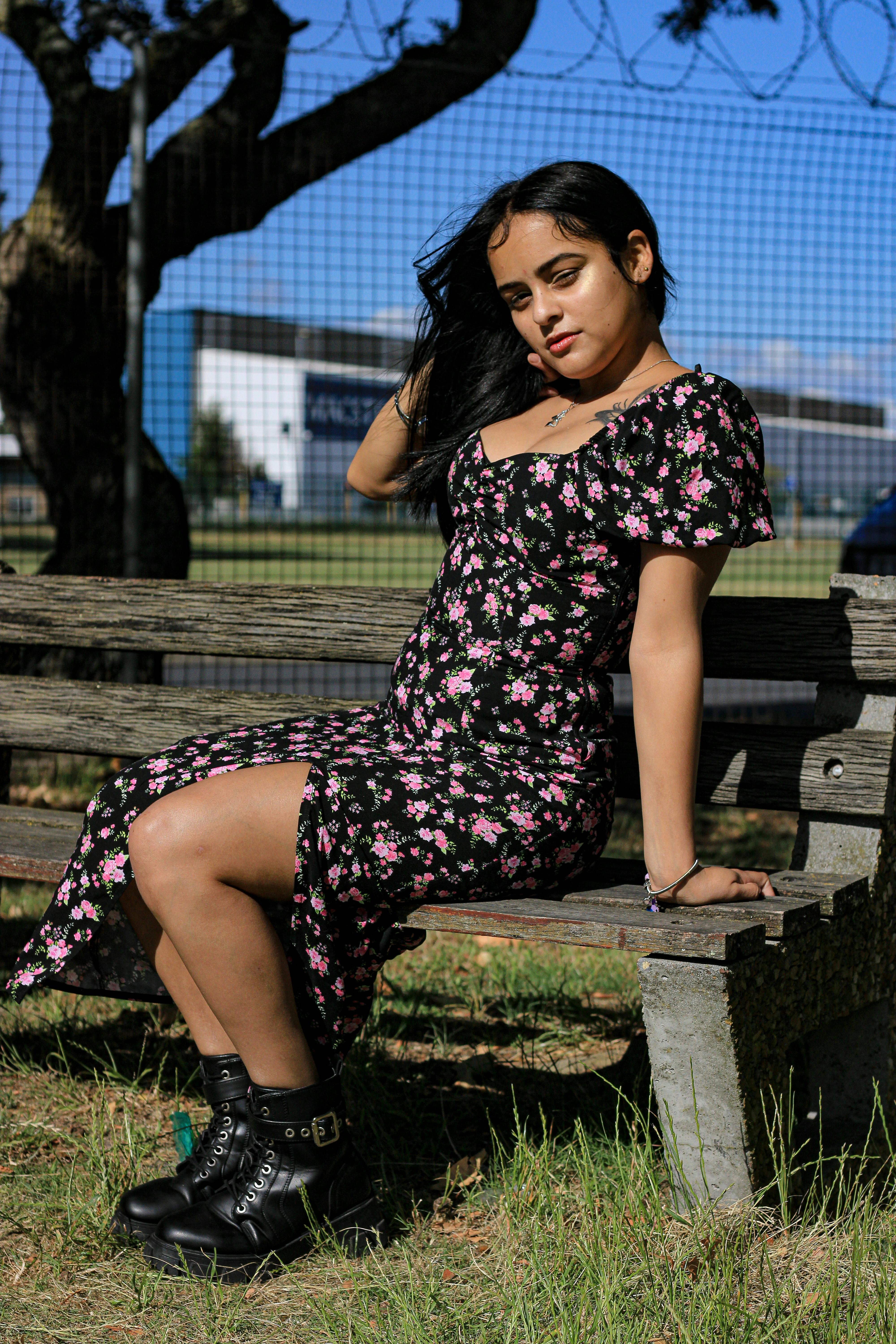 Woman sitting on bench in floral dress, enjoying a sunny day outdoors.