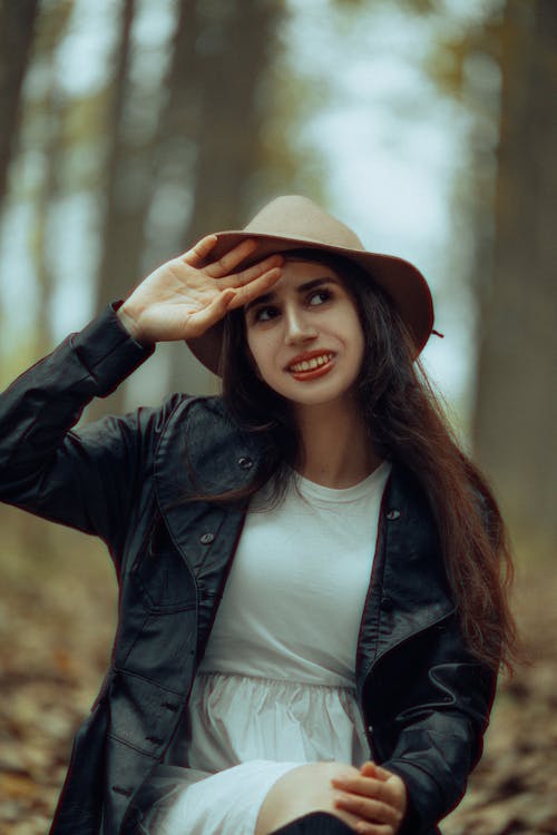 Young Woman in a Dress and Hat Sitting in a Park in Autumn and Smiling 