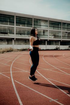 A woman in sportswear exercising by jumping rope on an outdoor track.