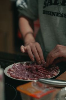 Close-up of hands arranging raw meat slices on a plate indoors, dim lighting.