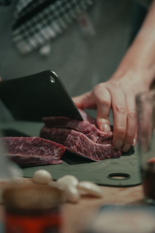 Free Close-up of hands slicing beef with cleaver on cutting board, capturing culinary preparation. Stock Photo