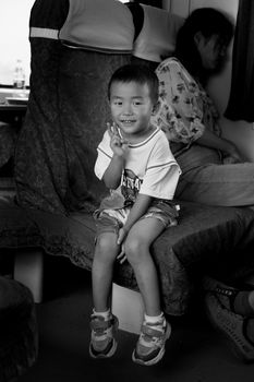 A young boy smiling and making a peace sign while sitting on a train seat.