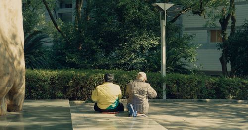 Free Two adults seated in a serene park surrounded by greenery on a sunny day. Stock Photo