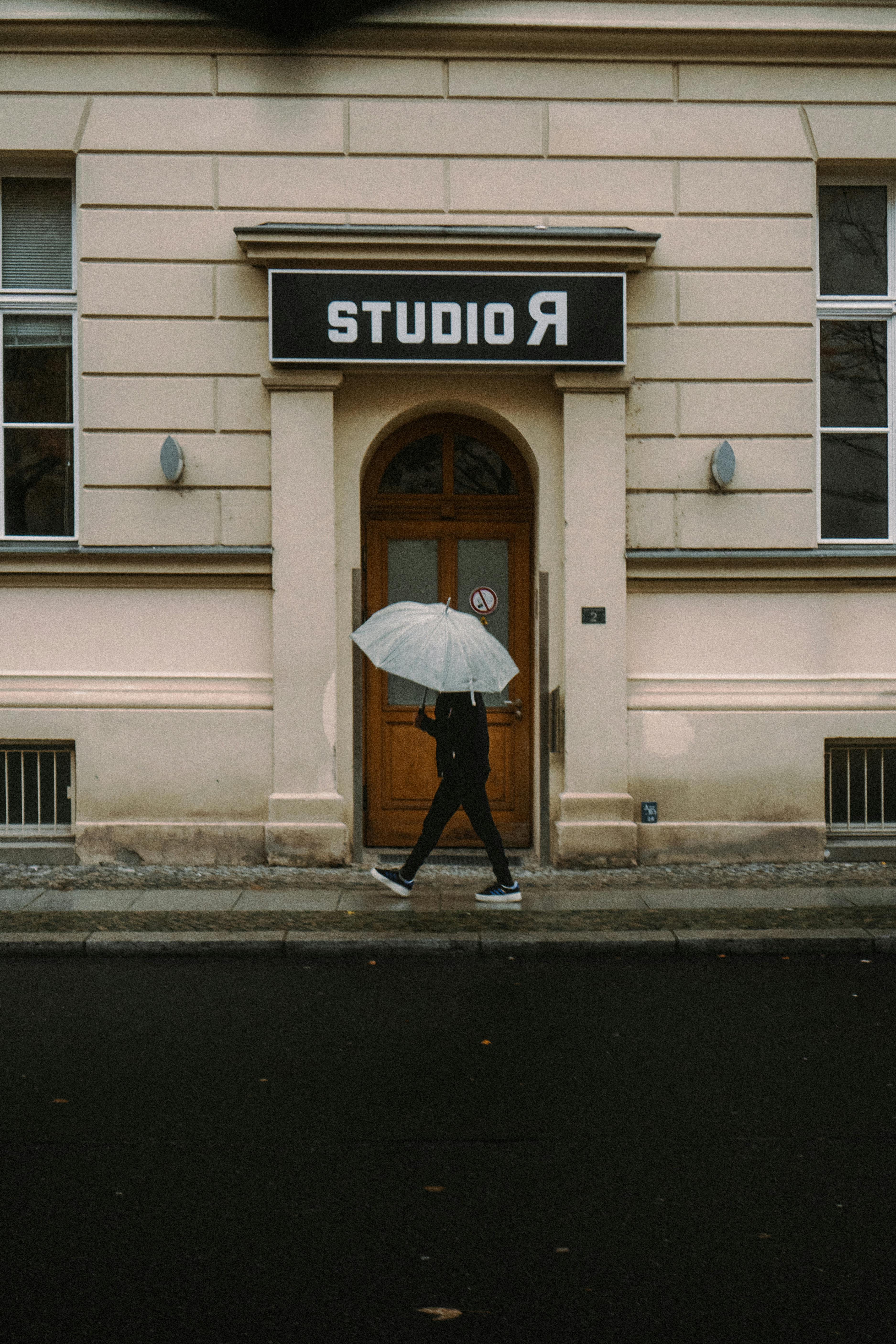 A person with an umbrella walks past studio facade in Berlin, Germany on a rainy day.