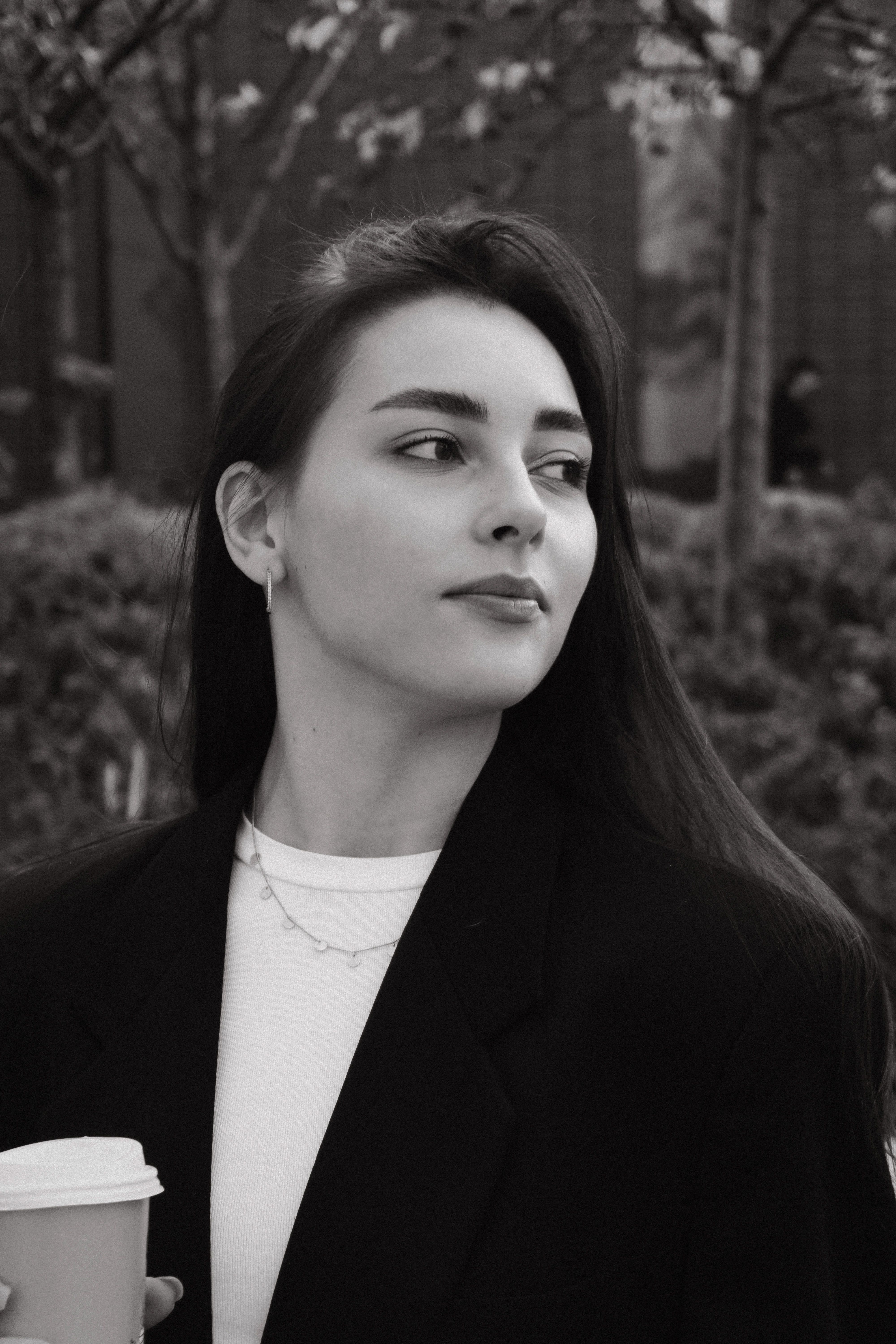 Black and white portrait of a stylish young woman holding a disposable cup outdoors.