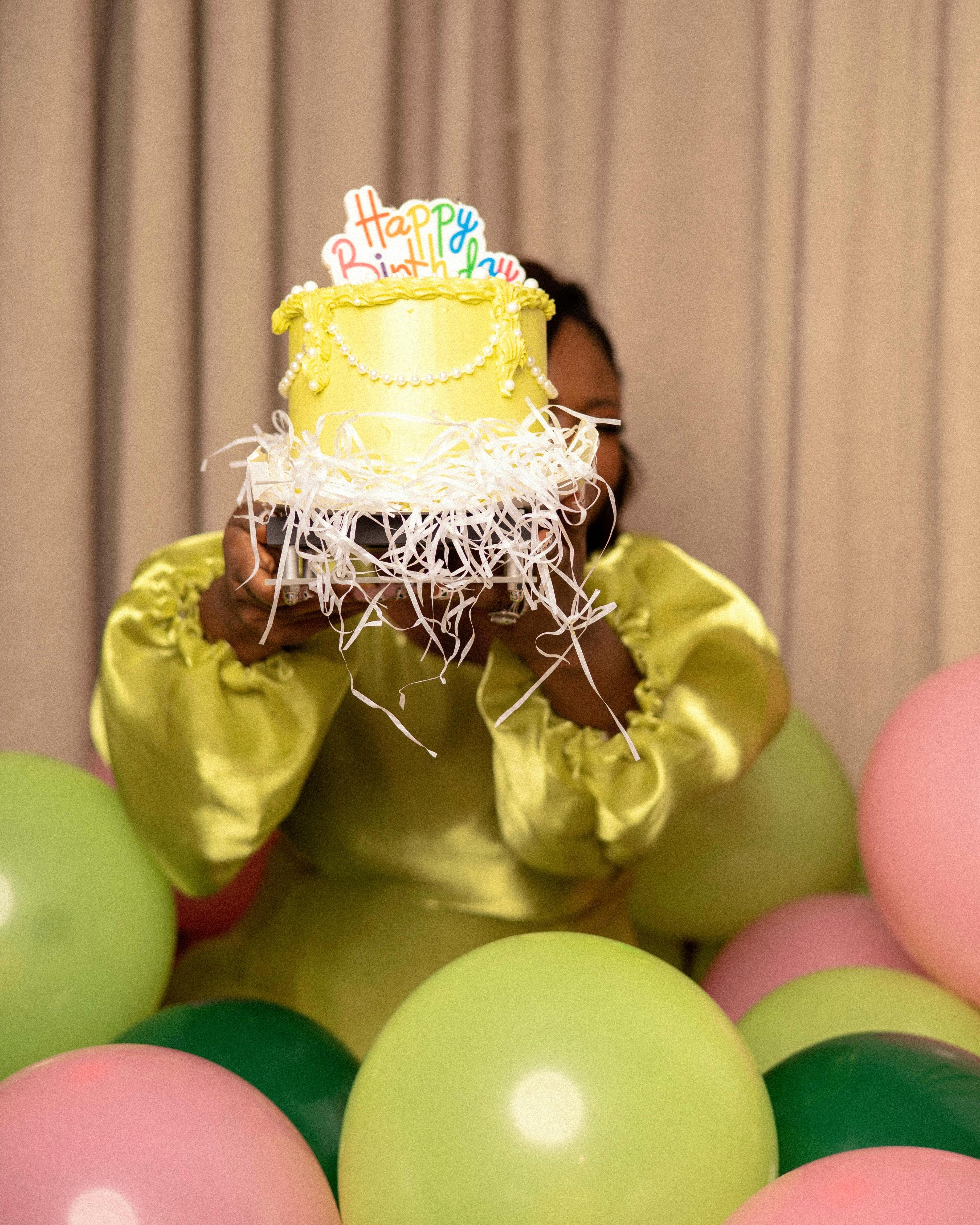 Bright birthday scene with girl holding cake surrounded by colorful balloons.