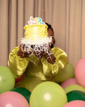 Bright birthday scene with girl holding cake surrounded by colorful balloons.