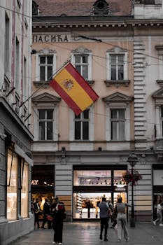 A lively street in Belgrade featuring a Spanish flag and historic architecture.