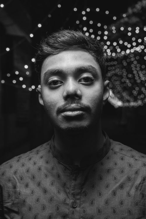 Free Monochromatic portrait of a young man with festive lights in the background, captured at night. Stock Photo