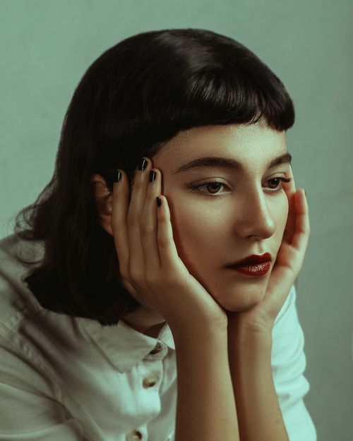 Free A thoughtful brunette woman with hands on cheeks, captured in a soft light portrait. Stock Photo