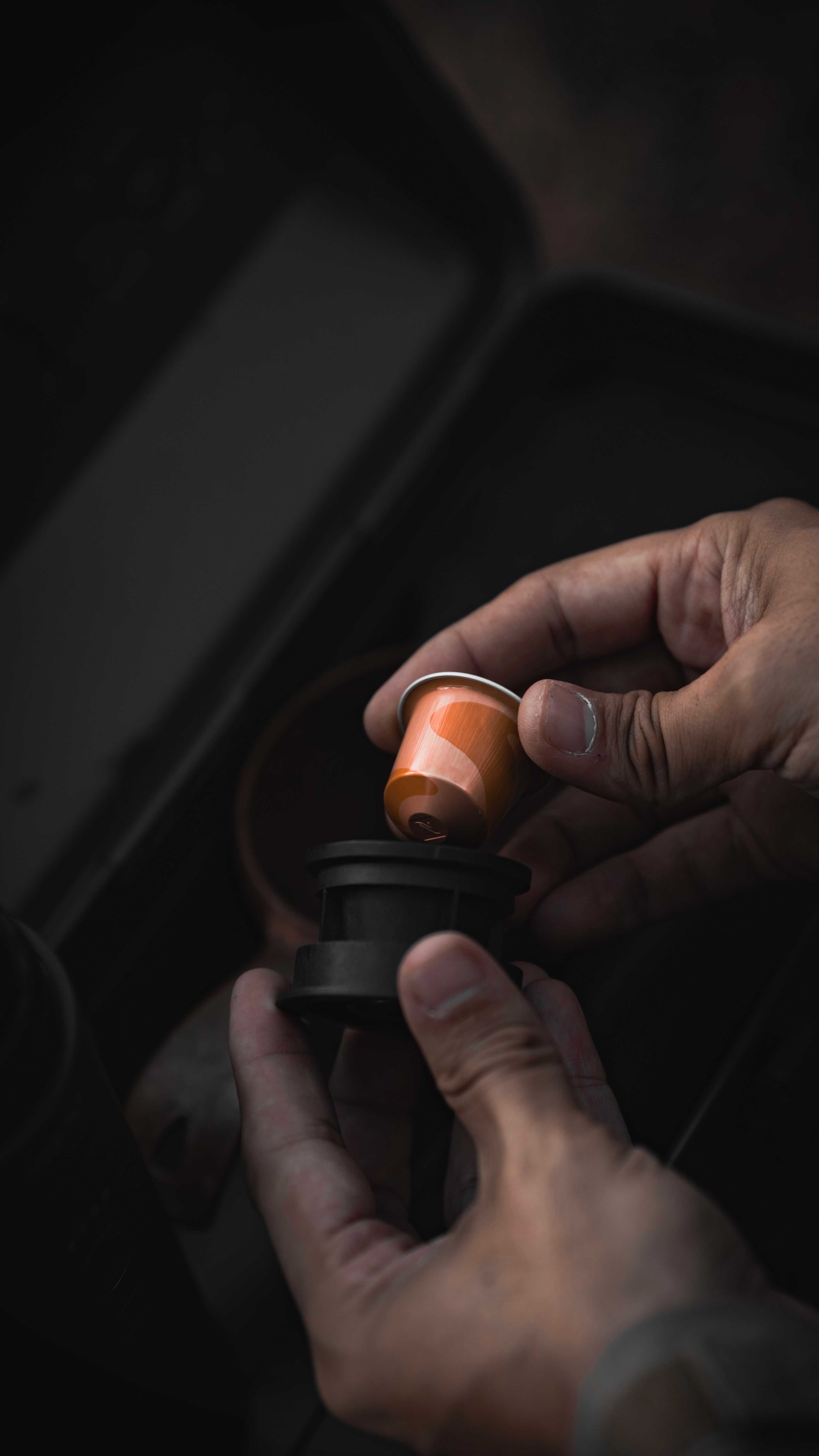 Close-up of a person inserting a coffee capsule into a machine, emphasizing hands and tactile interaction.