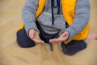 A child plays with sand on a beach in Egypt, showcasing a vibrant yellow vest.