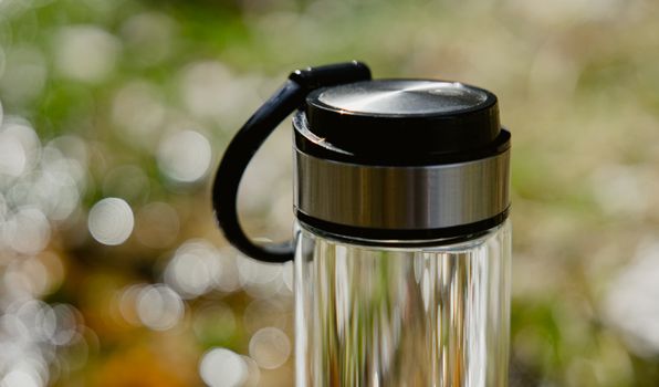 A glass water bottle with a black lid sitting on a table