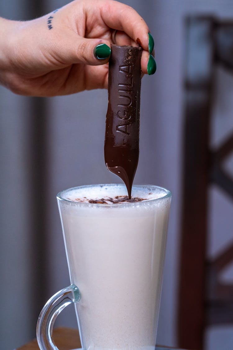 Close-up Of Woman Putting Chocolate Into A Glass With Foamed Milk 