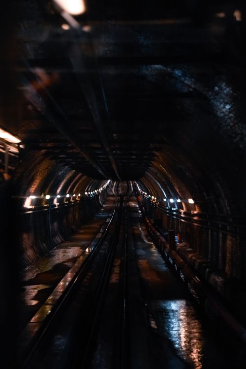 Free A dark underground tunnel with symmetrical illumination and wet reflections creating a dramatic perspective. Stock Photo