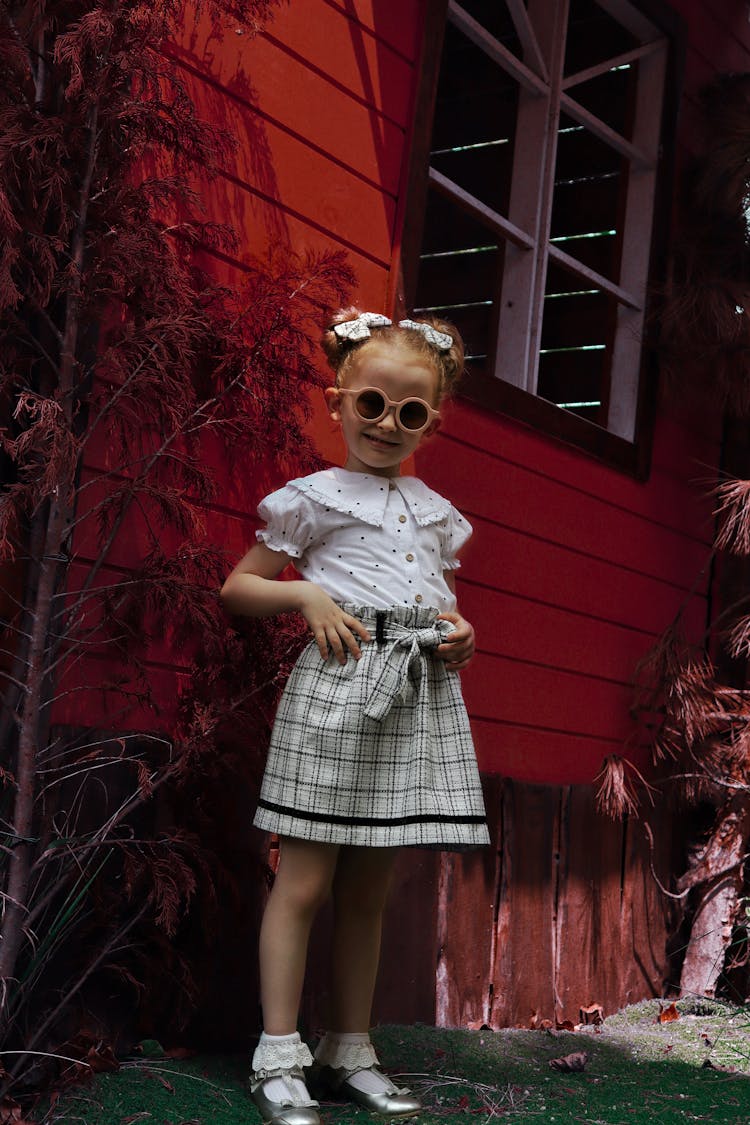 A Little Girl In A Skirt And Sunglasses Standing And Smiling 