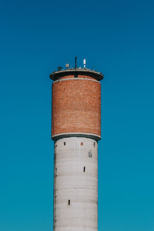 Free A large industrial water tower set against a clear blue sky, showcasing its brick and cement construction. Stock Photo