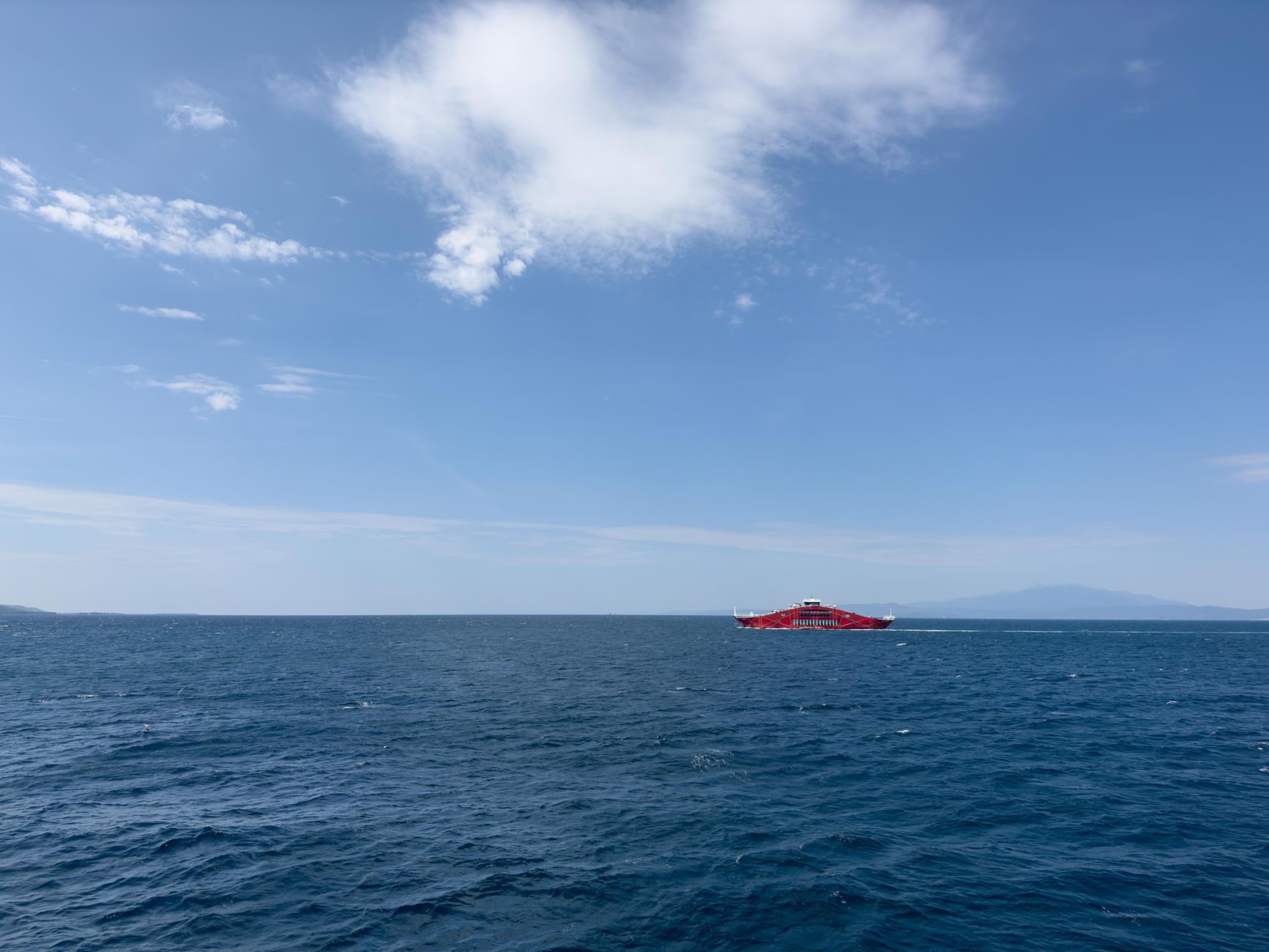 Red car ferry crossing the calm blue Aegean near Keramoti, the kind of boat used for Greek island hopping