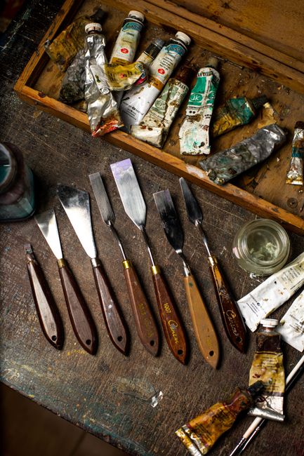 A top view of artistic palette knives and used paint tubes on a wooden table in a workshop.