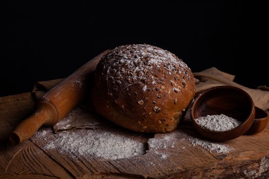 Rustic loaf of fresh seeded bread with flour in a dark, moody setting.