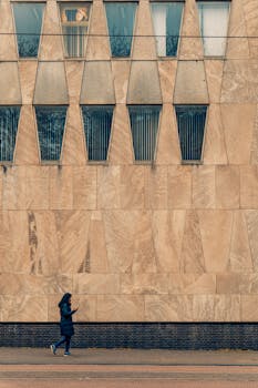 A woman in a black coat walks past a geometric stone building in The Hague, Netherlands, showcasing urban architecture.