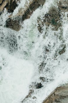 Aerial view of a powerful waterfall cascading over rocks, creating a foamy texture.