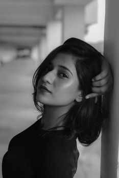 Graceful black and white portrait of a young woman leaning against a wall.