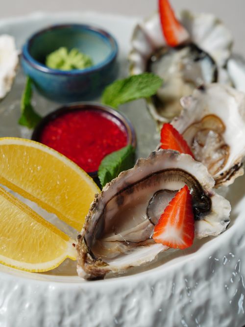 Free Close-up of fresh oysters garnished with lemon slices and strawberries, perfect for seafood lovers. Stock Photo