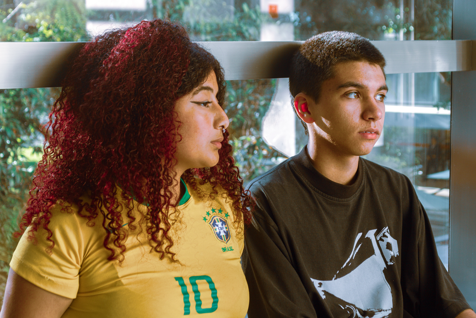 Teens sitting side by side indoors, enjoying the natural window light, showcasing friendship.