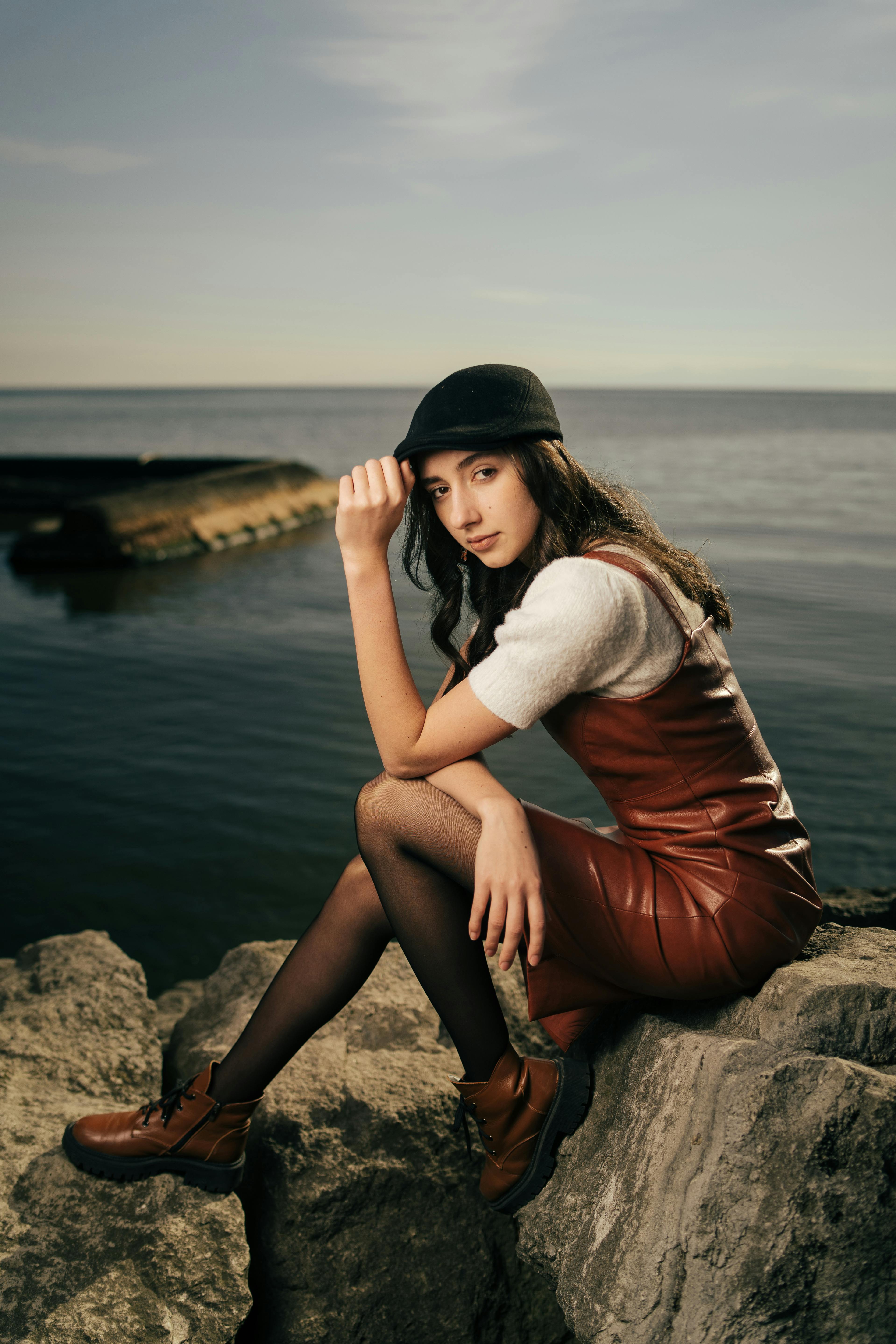 a woman in a leather dress and hat sitting on rocks by the water