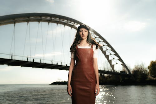 A woman in a brown leather dress standing in front of a bridge