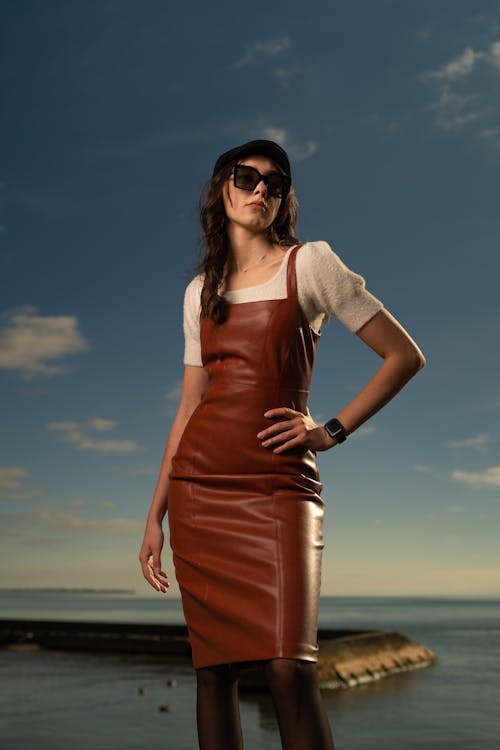 A woman in a leather dress and sunglasses standing by the water