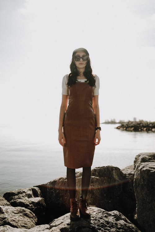 A woman standing on rocks wearing a brown dress