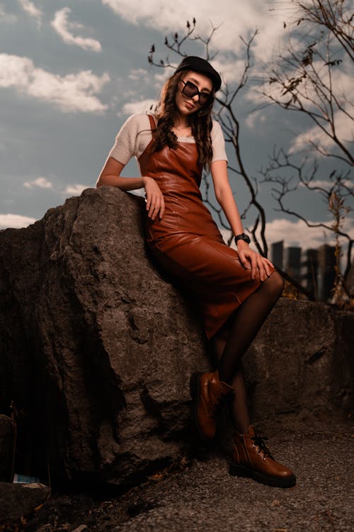 A woman in a leather dress and hat posing on a rock