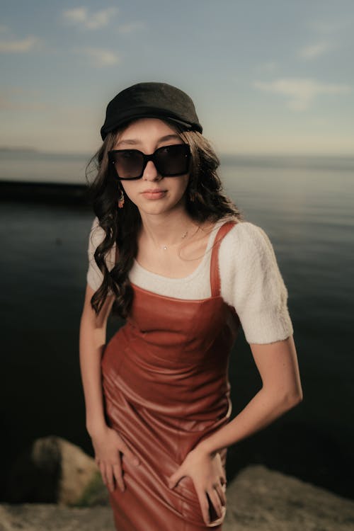 A woman in a leather dress and hat posing by the water