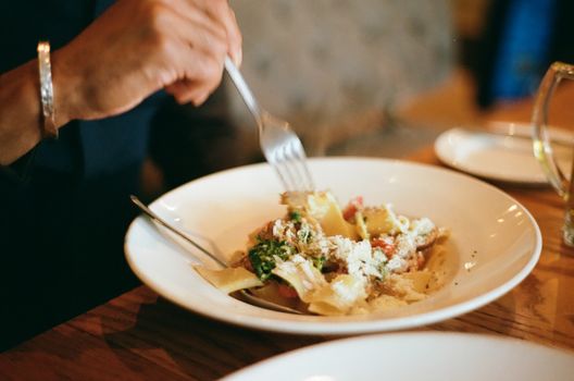 A person enjoying a comforting bowl of pappardelle pasta topped with parmesan and vegetables.