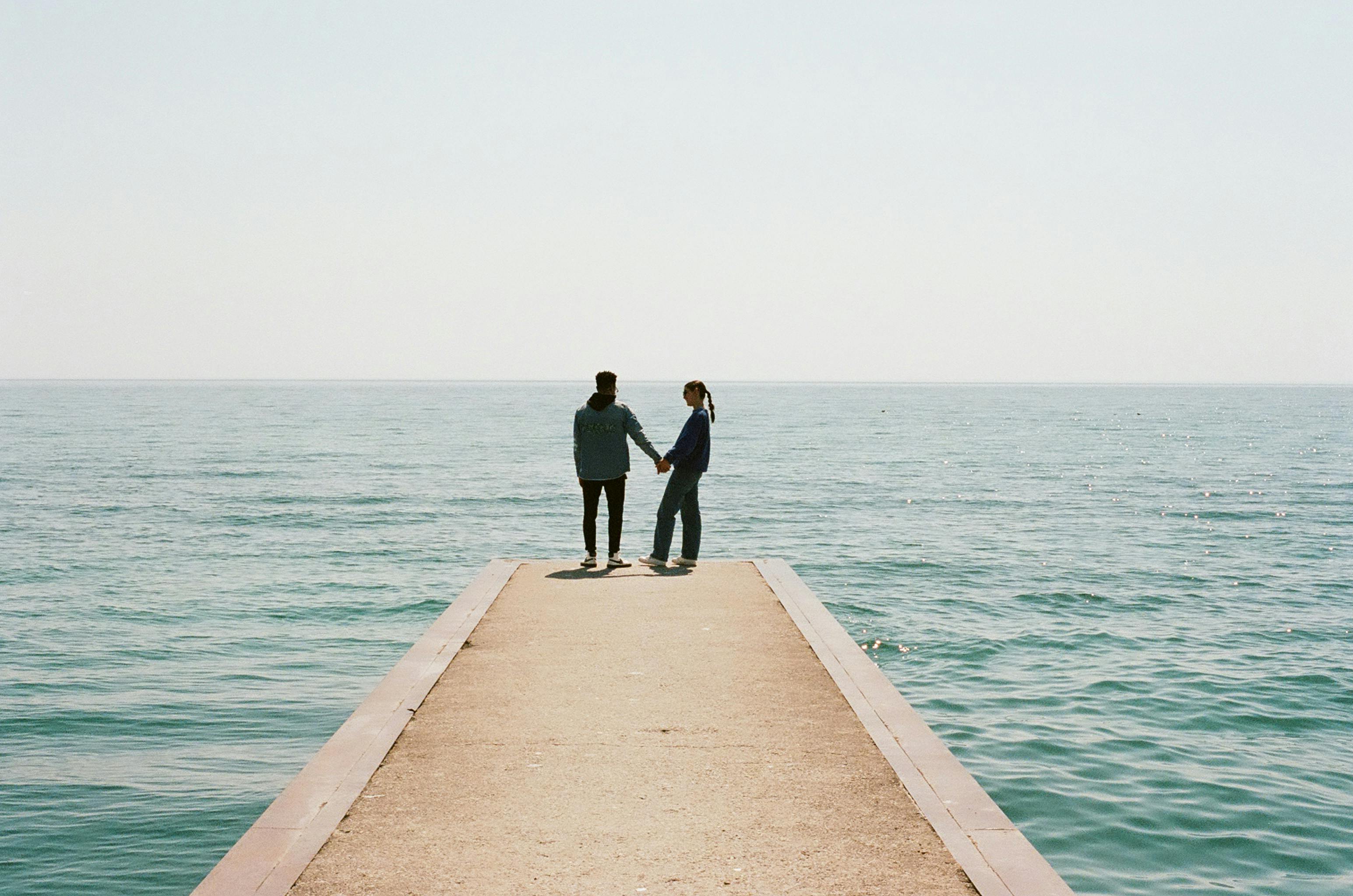 A couple holding hands on a pier by the sea, capturing a serene romantic moment.