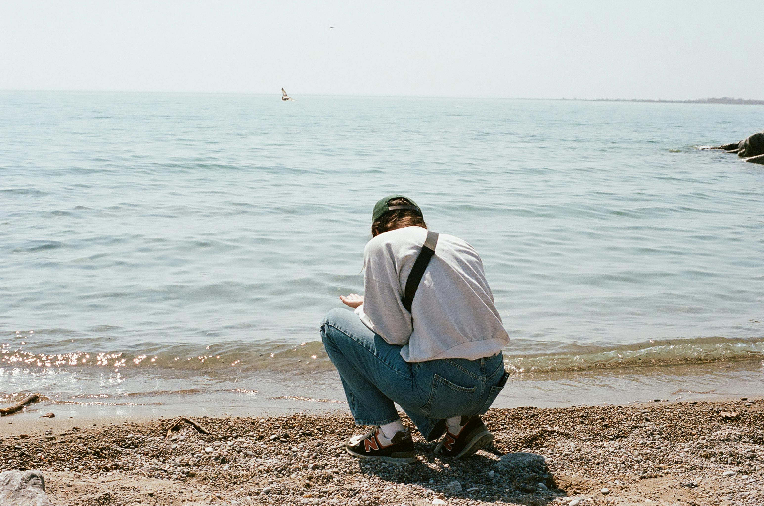 A person crouching on a serene beach shore, enjoying the peaceful ocean view.