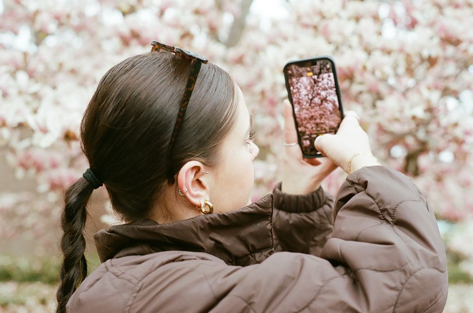 A woman capturing cherry blossoms on her smartphone during a spring day.