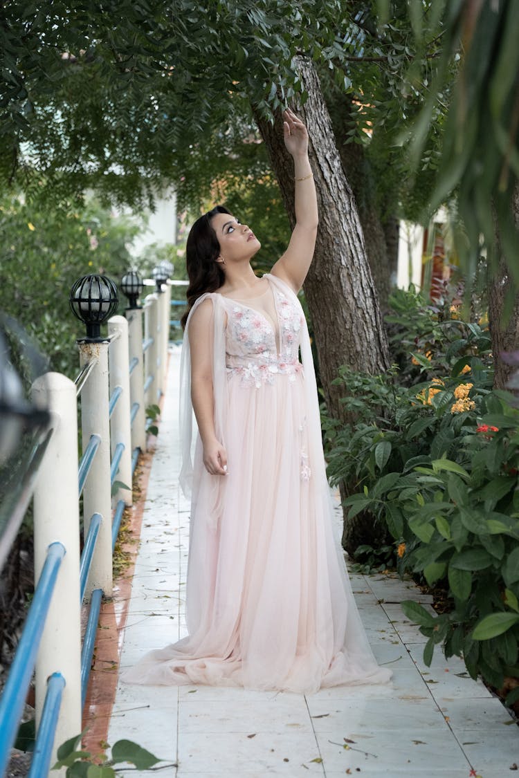 Woman In A Long White Gown Standing And Reaching Up For A Tree Branch 