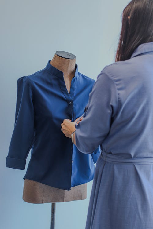 Woman Buttoning a Blue Stand-up Collar Shirt on a Bust 