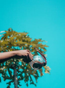 一只优雅的手从户外的玻璃壶中倒出咖啡，背景是充满活力的蓝天和树木