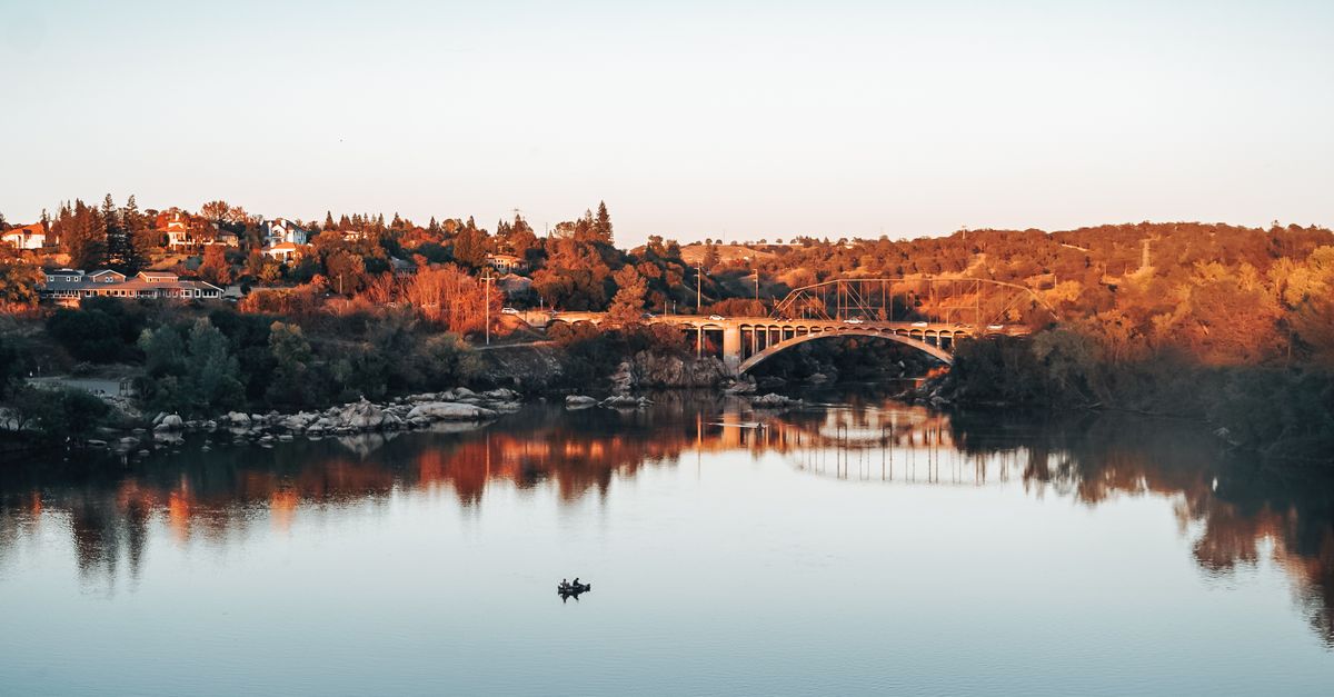 Beautiful sunset view of Rainbow Bridge spanning Lake Natoma surrounded by lush autumn foliage in California.