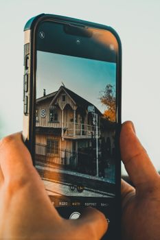 Hands holding smartphone capturing rustic house facade with warm tones.