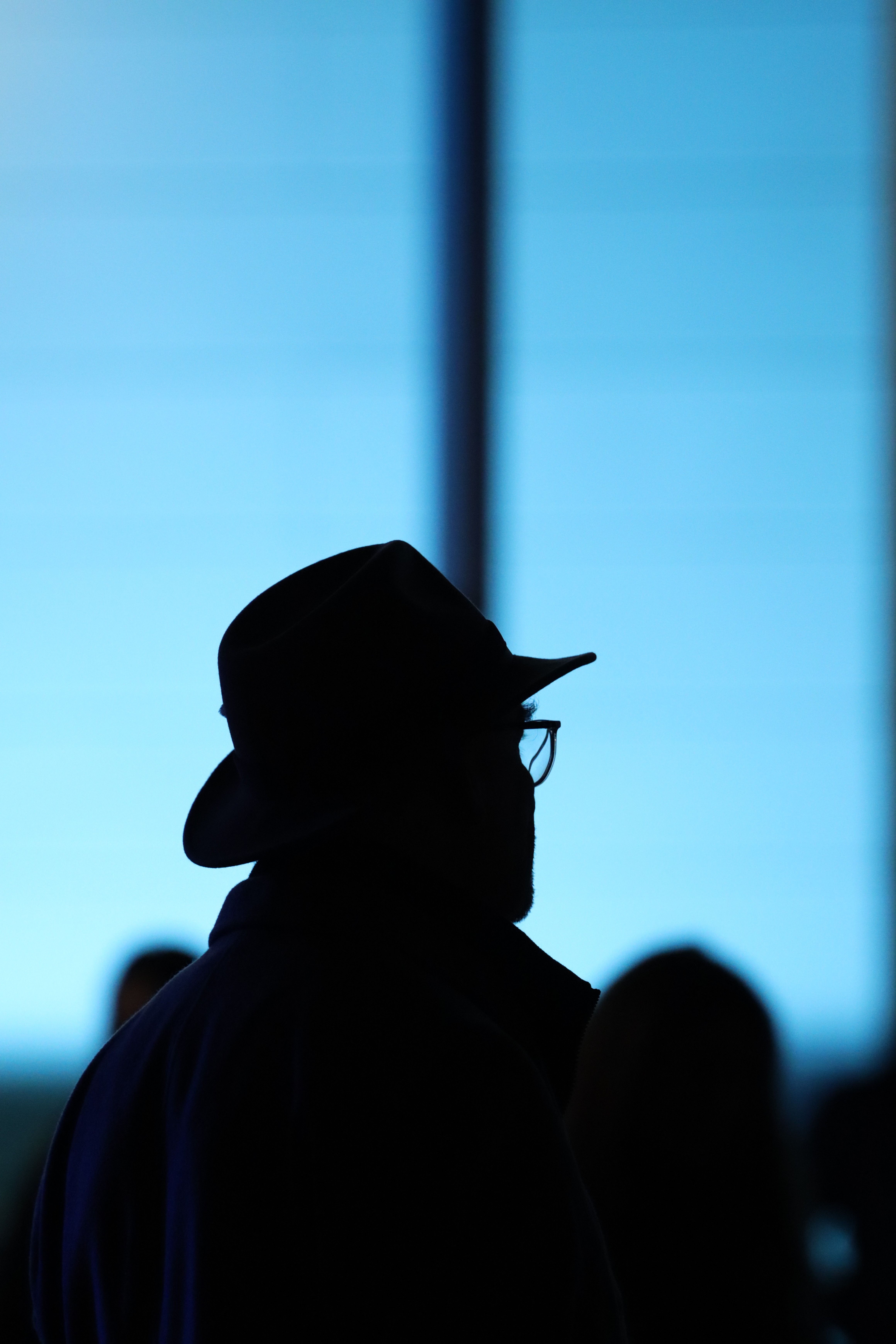 Silhouette of a man in hat and eyeglasses against a bright blue background, creating a mysterious scene.