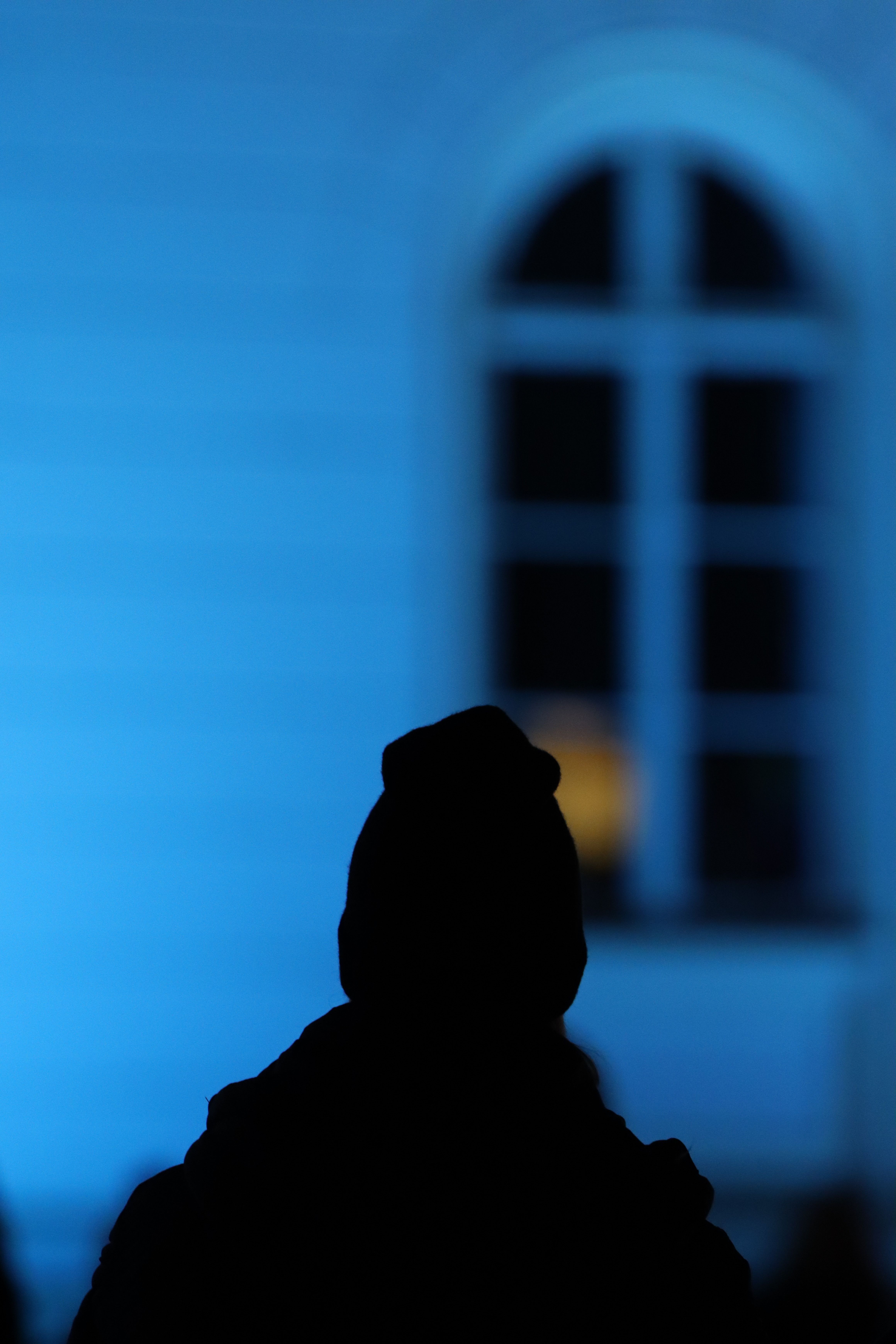 Silhouette of a person in front of a glowing blue-lit window during twilight in Jönköping, Sweden.