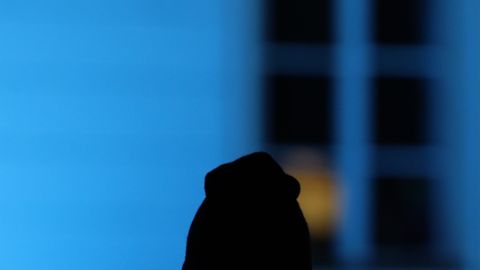Silhouette of a person in front of a glowing blue-lit window during twilight in Jönköping, Sweden.