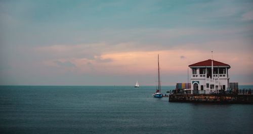 Free Calm sea with a harbor structure and distant sailboats under a dawn sky. Stock Photo