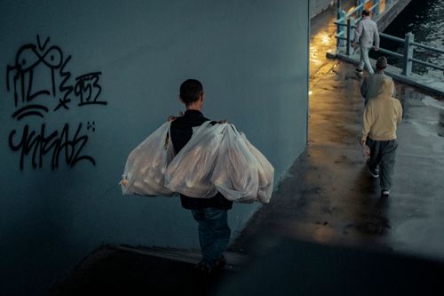 Free A person carrying plastic bags walks past graffiti in a dimly lit city street. Stock Photo